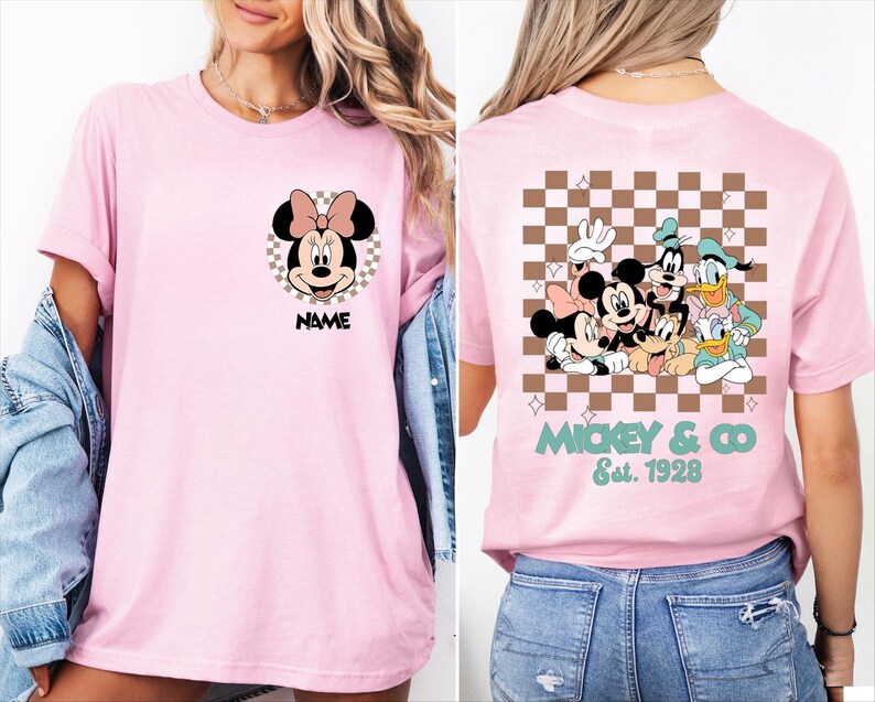 Puede incluir: Una camiseta rosa claro con un gr&aacute;fico de Minnie Mouse dentro de un c&iacute;rculo a cuadros y el texto NAME al frente. La parte posterior muestra un gran cuadrado a cuadros marr&oacute;n y blanco con Mickey, Minnie, Goofy, Donald y Pluto, con el texto MICKEY & CO Est. 1928.