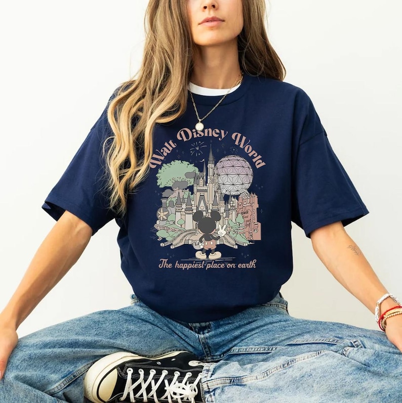 May include: Navy blue t-shirt featuring a colorful graphic of Walt Disney World with Mickey Mouse. The design includes a castle, Spaceship Earth, and the text "Walt Disney World" and "The happiest place on earth."