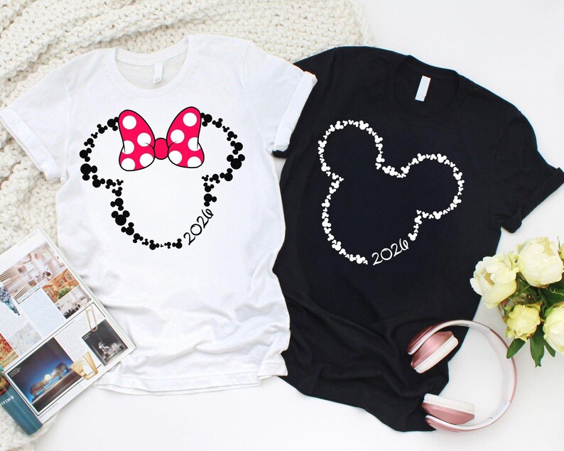 May include: A white t-shirt featuring a black outline of a mouse head shape filled with small mouse icons, a pink and white polka dot bow, and the text 2026, alongside a black t-shirt with a white mouse head outline and the text 2026.