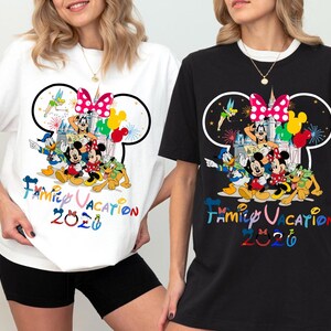 May include: A white t-shirt and a black t-shirt, each featuring a graphic of Disney characters including Mickey Mouse, Minnie Mouse, Donald Duck, Goofy, Pluto, and Tinker Bell. The design includes a castle, balloons, and the text Family Vacation 2026.