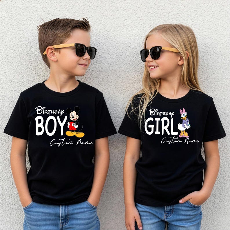 Pode incluir: Duas camisetas pretas com texto branco e personagens de desenhos animados. A camiseta da esquerda mostra o Mickey Mouse com o texto Birthday Boy e Custom Name. A da direita mostra a Margarida com o texto Birthday Girl e Custom Name.