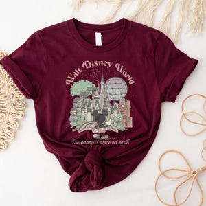 May include: Burgundy t-shirt featuring a graphic of Walt Disney World with Mickey Mouse. The design includes the castle, Spaceship Earth, and the text "Walt Disney World" and "The happiest place on earth".