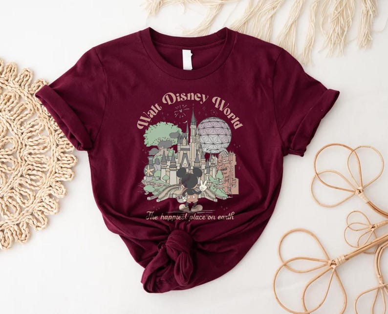 May include: Burgundy t-shirt featuring a graphic of Walt Disney World with Mickey Mouse. The design includes the castle, Spaceship Earth, and the text "Walt Disney World" and "The happiest place on earth".