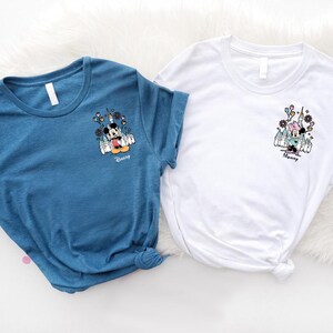 May include: A blue t-shirt and a white t-shirt, each featuring a small graphic on the left chest. The blue shirt displays Mickey Mouse with the text "Daddy" below, while the white shirt shows Minnie Mouse with the text "Mommy" below.