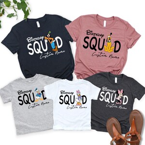Pode incluir: Cinco camisetas de manga curta nas cores azul marinho, malva, cinza claro, branco e cinza chumbo. Cada camiseta apresenta o texto "Birthday SQUAD" com um personagem da Disney substituindo a letra A, incluindo Pateta, Pluto, Pato Donald, Margarida e Minnie.