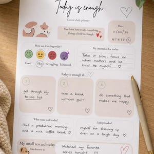 Op de afbeelding: Een dagplanner met de tekst "Today is enough" en prompts voor gevoelens, intenties en beloningen. De planner bevat ruimte voor een to-do lijst, zelfreflectie en een koffiepauze. Een pen ligt op de pagina.