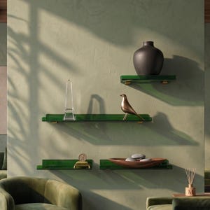 May include: Four dark green floating shelves mounted on a wall. The top shelf holds a matte black vase. The middle shelf features a clear glass obelisk and a metallic bird figurine. The bottom shelves hold a small gold object and a brown bowl with stones.