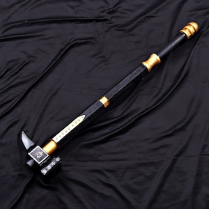 May include: A long-handled war hammer featuring a black shaft with gold-colored accents and a pommel. The hammer head includes a silver-toned spike, a square face with a white emblem, and a side panel decorated with a row of small white cross symbols.