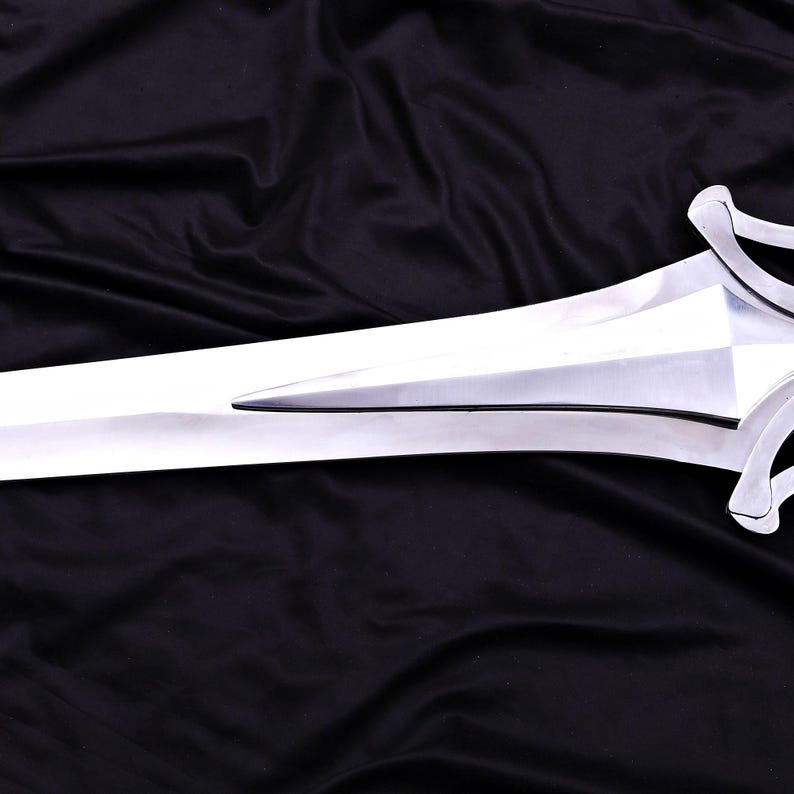 May include: A polished, silver-colored sword with a double-edged blade. The hilt features a decorative, curved design. The sword is displayed against a black fabric background.