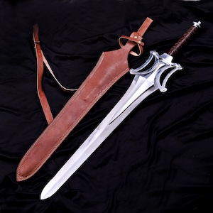 May include: A silver sword with a brown leather-wrapped handle and a matching leather sheath. The sword has a distinctive blade shape and a guard with decorative cutouts. The sheath includes a shoulder strap.