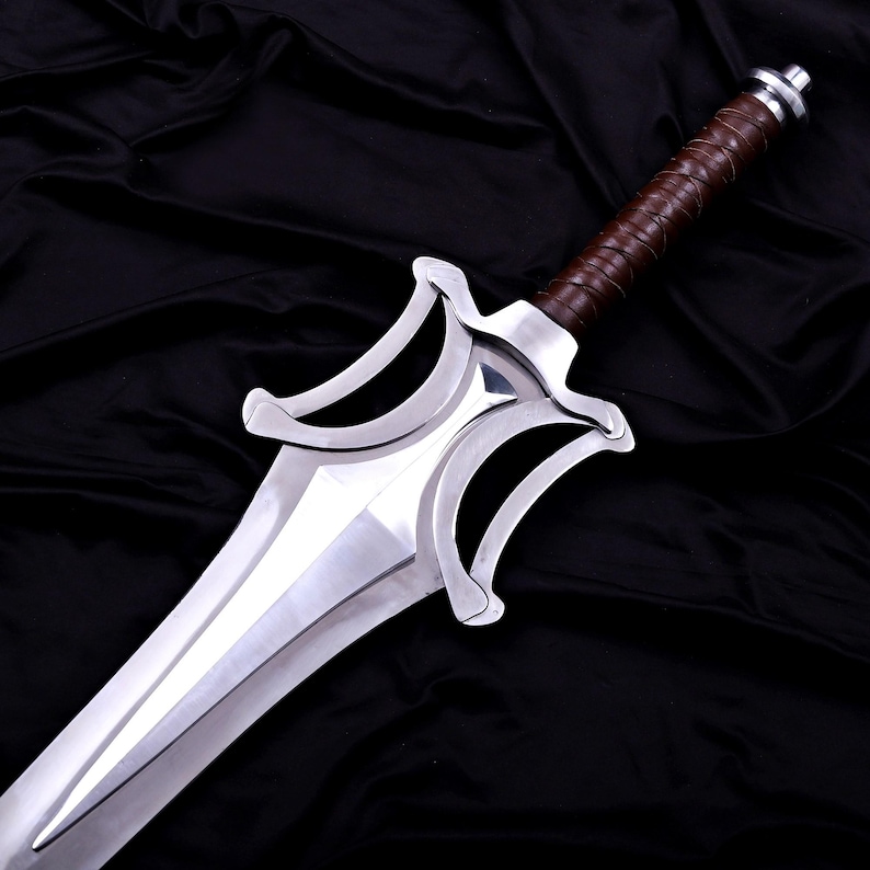 May include: A polished silver sword with a brown leather-wrapped handle. The blade is wide and has a distinctive shape with curved edges. The handle is wrapped in brown leather. The sword is displayed against a black background.