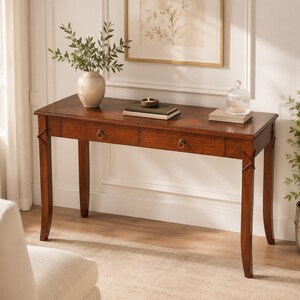 May include: A dark brown wooden console table with two drawers and brass hardware. The table has a rectangular top and four curved legs. A vase with greenery, books, and a decorative glass jar sit on top. The table is 60 inches long.