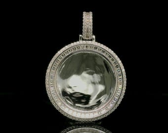 Può includere: Un ciondolo circolare color argento con un disco centrale liscio e riflettente, incorniciato da un doppio bordo di piccole pietre chiare rettangolari taglio baguette e un anello esterno di minuscole pietre chiare rotonde.