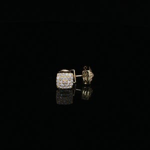 May include: A pair of square-shaped stud earrings in a gold-tone metal finish. Each earring features a cluster of small, clear, sparkling stones set across the front face, creating a textured, reflective surface that catches the light.