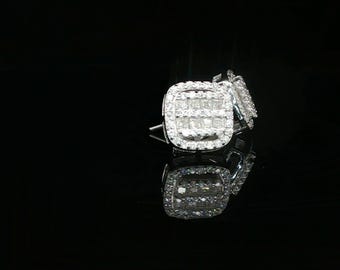 Può includere: Un paio di orecchini a lobo quadrati con un gruppo centrale di pietre taglio princess circondate da un alone di pietre più piccole taglio brillante rotondo. Gli orecchini sono realizzati in metallo color argento lucido e riflettente.