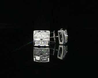 Può includere: Un paio di orecchini a lobo di forma quadrata realizzati in metallo lucido color argento. Ogni orecchino presenta un gruppo di quattro pietre trasparenti taglio princess disposte a griglia, creando una superficie brillante e riflettente su sfondo scuro.