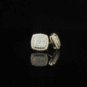May include: A pair of square-shaped gold stud earrings featuring a central cluster of small, clear, round-cut stones surrounded by a halo of additional clear stones. The earrings have a polished gold metal frame and a reflective, metallic finish.