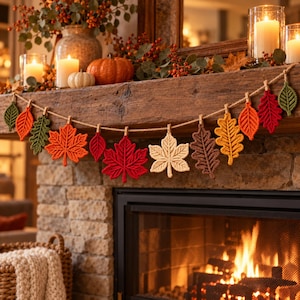 May include: A decorative garland featuring various crocheted leaves in shades of red, orange, yellow, brown, and green. The leaves are attached to a natural jute twine string with small wooden clothespins, creating a seasonal autumn display.