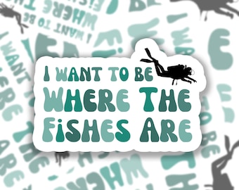 May include: A sticker with a blue, green, and white gradient design. The sticker features a scuba diver and the text "I want to be where the fishes are".
