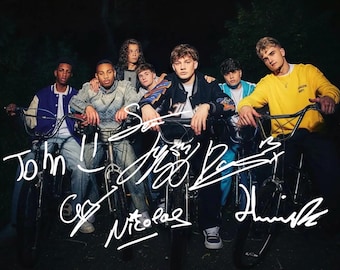 May include: A group of people on bicycles, set against a dark backdrop. They are dressed in diverse attire, including jackets and sweaters. The image features handwritten signatures across the front.