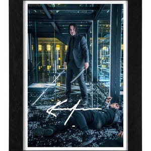 May include: A framed print featuring a scene from a film with a man in a dark suit holding a sword standing over another person lying on a floor covered in glass shards. A white signature is written across the centre of the image.