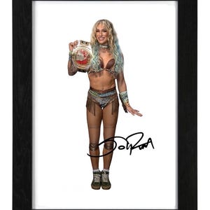 May include: A framed photograph of a blonde wrestler with blue-streaked hair, wearing a brown fringed two-piece outfit, holding a championship belt, and wearing olive high-top sneakers. The image features a black signature across the lower portion.