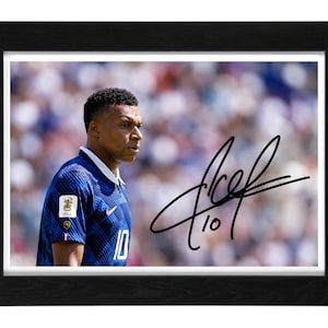 Peut inclure: Une photographie encadrée d'un joueur de football portant un maillot bleu avec le numéro 10 et un col blanc. Le joueur est représenté de profil sur un fond de stade flou. Une signature à l'encre noire et le numéro 10 sont visibles sur l'image.