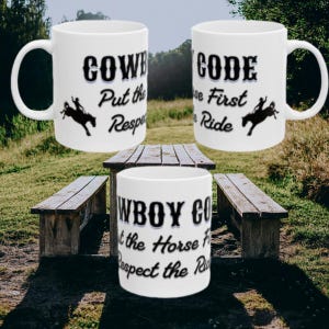 Può includere: Tre tazze in ceramica bianca con testo nero e una silhouette di una persona che cavalca un cavallo imbizzarrito. Il testo recita Cowboy Code, Put the Horse First e Respect the Ride, in un carattere in grassetto dallo stile western.
