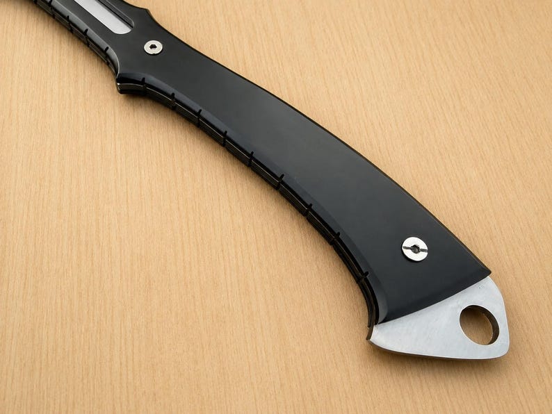 May include: A curved knife handle featuring a smooth matte black finish with a series of small vertical notches along the edge. The handle is secured with two silver-toned circular screws and terminates in a metallic pommel with a circular hole.