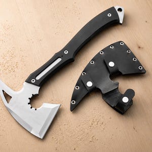 May include: A tactical hatchet with a silver-toned metal blade featuring a circular cutout and a triangular opening, paired with a black handle and a matching black sheath secured with silver-toned metal snaps and rivets.