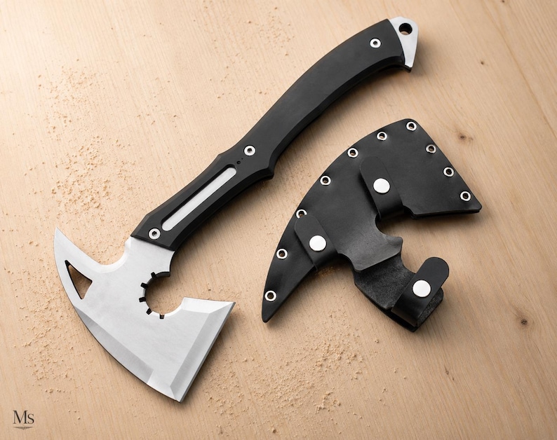 May include: A tactical hatchet with a silver-toned metal blade featuring a circular cutout and a triangular opening, paired with a black handle and a matching black sheath secured with silver-toned metal snaps and rivets.