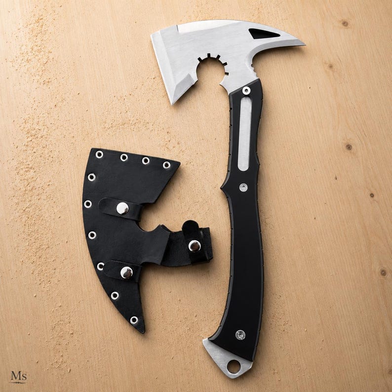 May include: A tactical hatchet with a silver-toned metal head featuring a notched blade and a pointed spike, attached to a black handle. A matching black leather sheath with silver metal rivets and snap closures is positioned next to the hatchet.