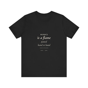 May include: Black t-shirt with white text that reads "memory is a flame passed hand to hand" with arrows and the dates 1939-1945. The shirt is made of a soft material.