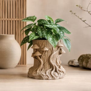 May include: A cylindrical planter with a textured exterior resembling a tree stump, featuring raised relief carvings of mushrooms and winding roots. A green and silver variegated pothos plant grows from the top of the tan-colored container.