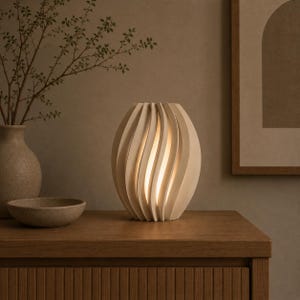 May include: A table lamp with a matte off-white, egg-shaped exterior featuring vertical, spiraling slats that reveal a warm, glowing light from within. The lamp has a structured, ribbed design that creates a soft illumination through the gaps.