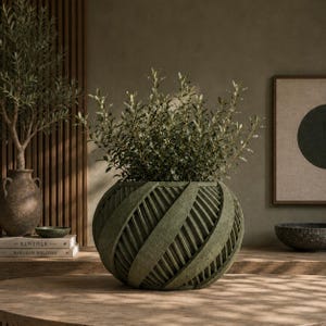 May include: A round, sage green planter with a textured, spiraling ribbon design. The planter features a wide, spherical body with deep, overlapping vertical grooves and contains a lush, leafy green plant with small, pointed foliage.