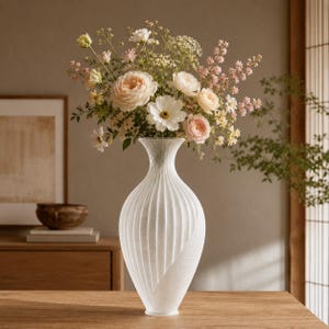 May include: A tall, white, translucent vase with a textured, spiraling ribbed pattern on its surface. The vase is filled with a large, colorful bouquet of various flowers, including pale pink, cream, and white blossoms with green stems.
