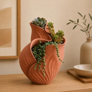 May include: A terracotta-colored ceramic planter with a multi-tiered, wavy, and ribbed exterior design. The planter holds a variety of succulents, including a string of pearls plant that cascades over the side and several upright green succulents.