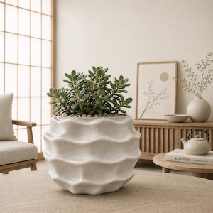 May include: A round, off-white ceramic planter with a textured, wavy, horizontal ripple pattern on its exterior. The planter is filled with a lush, green jade plant featuring thick, succulent leaves and small pebbles covering the soil surface.
