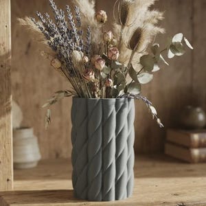 May include: A cylindrical gray vase with a vertical rope-like twisted texture. The vase is filled with a dried floral arrangement consisting of purple lavender sprigs, small pink rosebuds, fluffy pampas grass, brown teasels, and green eucalyptus leaves.