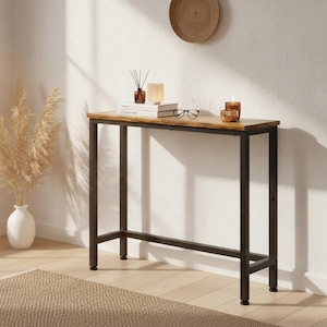 May include: A rectangular console table featuring a rustic brown wood-grain top and a sturdy black metal frame with four legs and a lower support bar. The table surface holds a stack of books, a glass candle holder, and a pair of black eyeglasses.