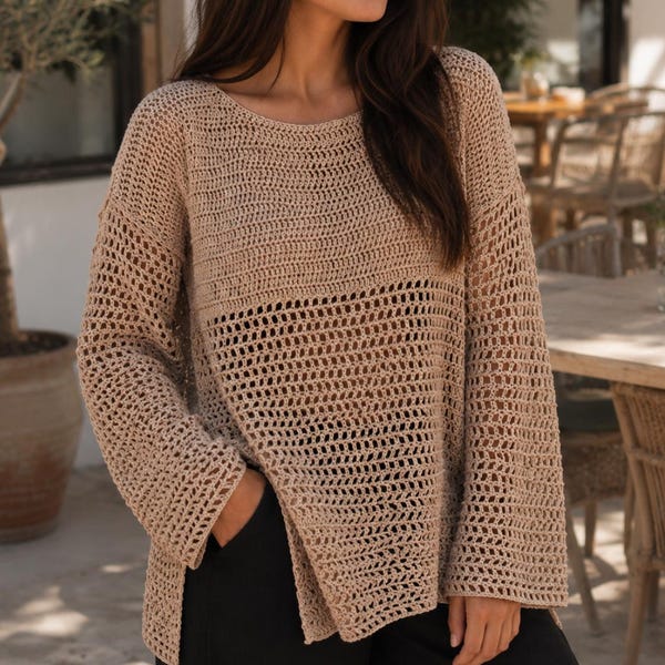 Könnte beinhalten: Ein beigefarbener, langärmeliger Häkelpullover mit einem lockeren, offenen Strickmuster an Körper und Ärmeln, einem weiten Rundhalsausschnitt und Seitenschlitzen am Saum, kombiniert mit einer schlichten schwarzen Hose.