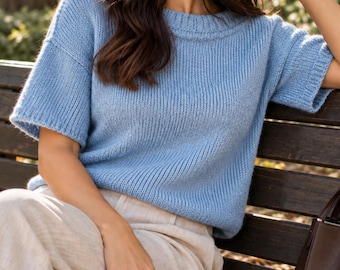 Könnte beinhalten: Ein hellblauer, kurzärmeliger Strickpullover mit geripptem Rundhalsausschnitt und gerippten Ärmelbündchen. Das Kleidungsstück hat eine lockere Passform mit überschnittenen Schultern und ein strukturiertes Strickmuster am gesamten Körper.