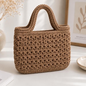 Peut inclure: Un sac à main rectangulaire en crochet marron moyen, doté d'un motif dense de points en forme d'étoile sur tout le corps. Le sac comprend deux anses en crochet intégrées et assorties sur le dessus ainsi qu'une base plate et structurée.