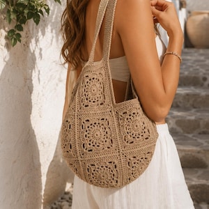 Puede incluir: Un bolso tote de ganchillo en color beige construido a partir de múltiples motivos cuadrados con intrincados patrones circulares. El bolso tiene dos asas integradas y una estructura flexible, mostrando una textura de hilo uniforme.