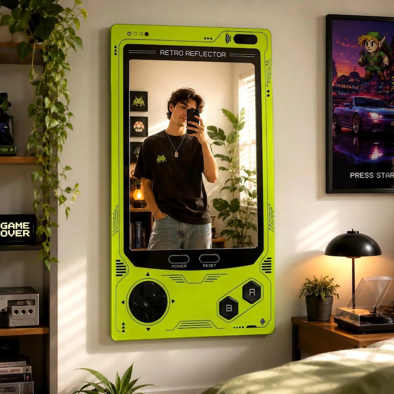 May include: A rectangular wall mirror designed to resemble a handheld gaming console in bright lime green. The frame features black directional buttons, A and B buttons, and power and reset labels. The top of the frame displays the text RETRO REFLECTOR.