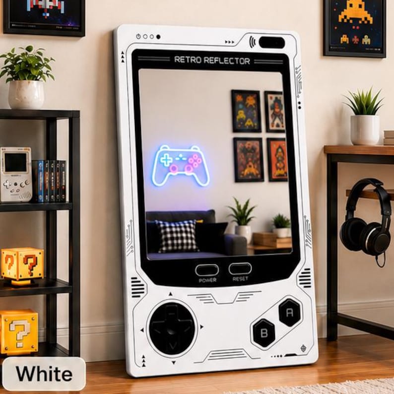 May include: A rectangular floor mirror designed to resemble a handheld gaming console. The white frame features black button graphics, a directional pad, and the text RETRO REFLECTOR. The mirror surface reflects a room with a neon game controller.