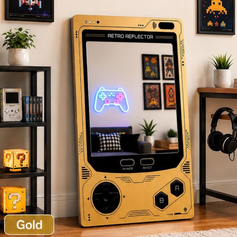 May include: A rectangular gold-colored mirror designed to resemble a handheld gaming console. The frame features black buttons, a directional pad, and the text RETRO REFLECTOR. The mirror surface reflects a room with a glowing neon game controller.