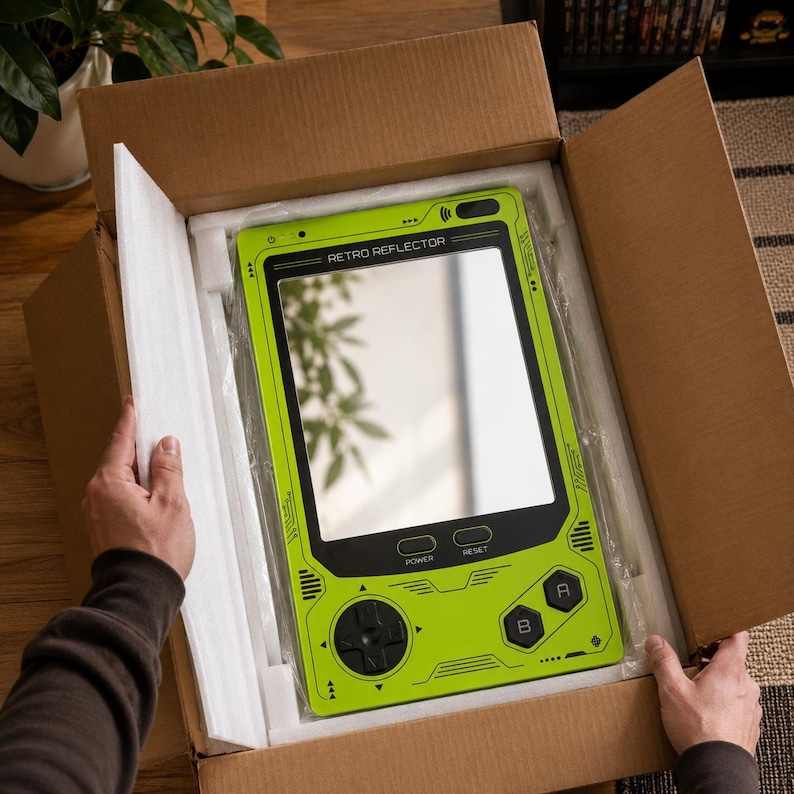 May include: A lime green rectangular mirror designed to resemble a handheld gaming console, featuring the text RETRO REFLECTOR at the top, a central reflective surface, a directional pad, two buttons labeled A and B, and power and reset buttons.