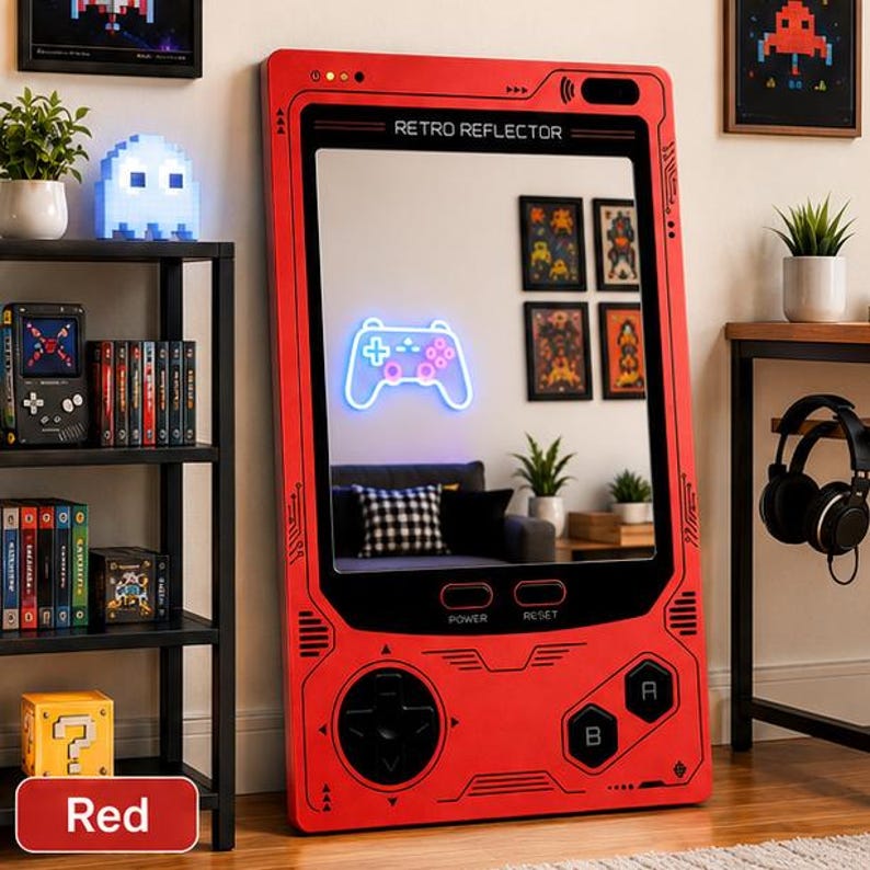 May include: A large, rectangular, red floor mirror designed to resemble a vintage handheld gaming console. The frame features black button graphics, a directional pad, and the text RETRO REFLECTOR at the top. The mirror surface reflects a room.
